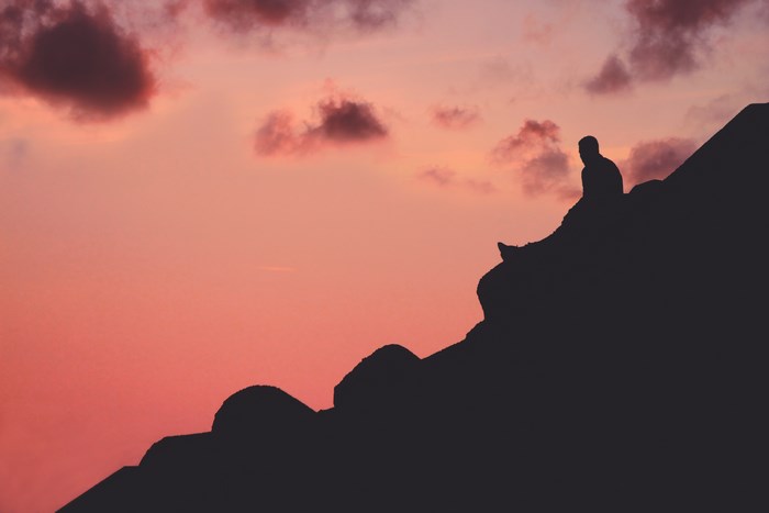 Silhouette of a person sitting on a ridge at sunset in Assilah