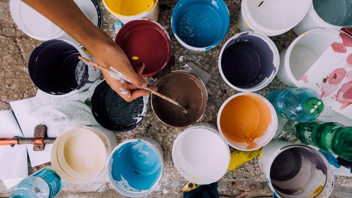 Artist's hand holding a paintbrush over colorful paint pots