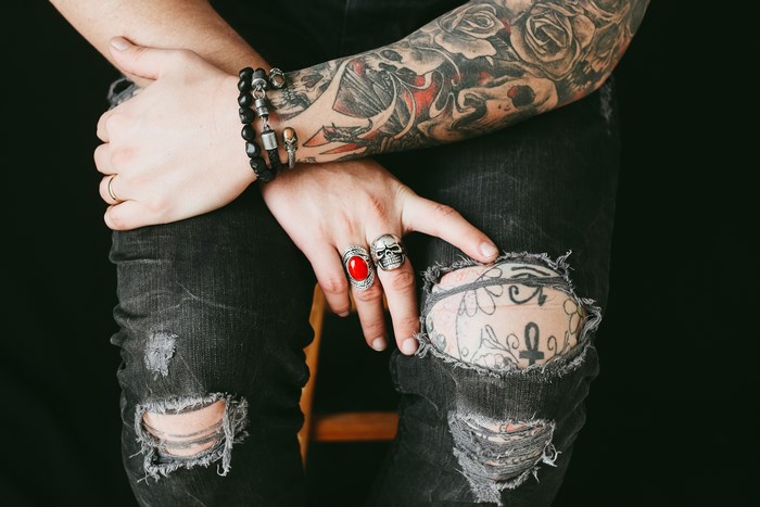 Person with tattoos and ripped jeans wearing rings and bracelet