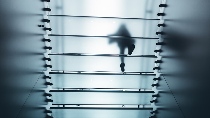 Silhouette of a person walking up a glass staircase