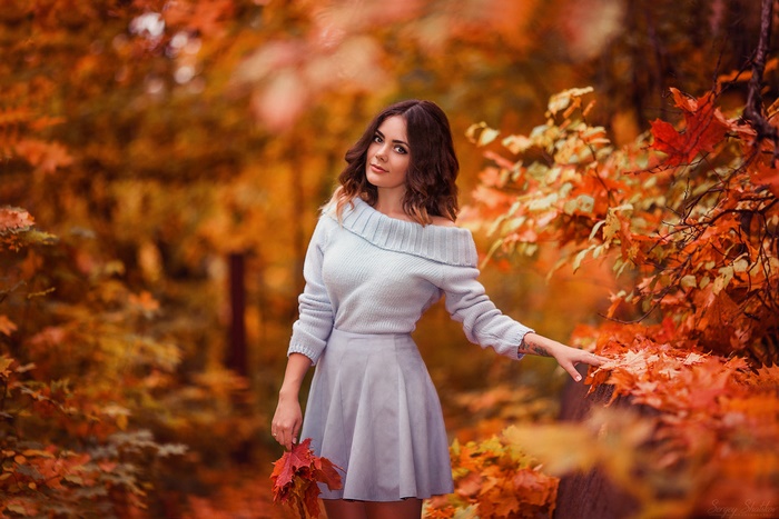 Woman in a light blue off-the-shoulder sweater and skirt holding leaves