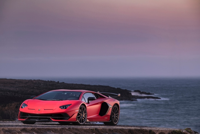 Red Lamborghini Aventador SVJ parked by the ocean at sunset