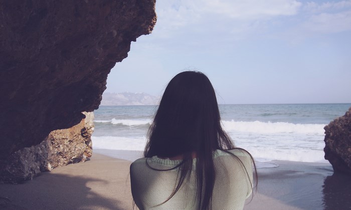 Woman looking at the sea from a rocky alcove on the beach