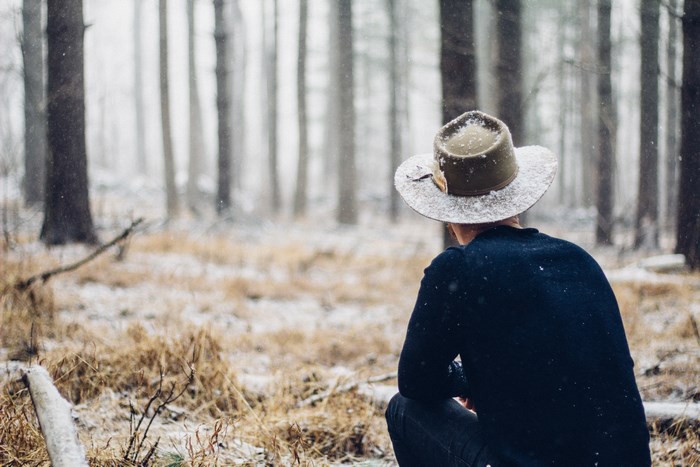 Man in hat squatting in snowy forest
