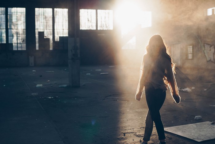 Girl walking in a sunlit abandoned warehouse