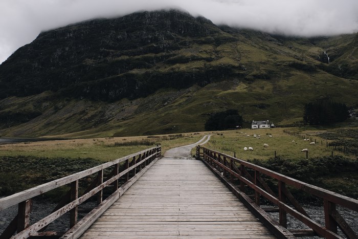 Wooden bridge leading to a farmhouse in a foggy mountain landscape