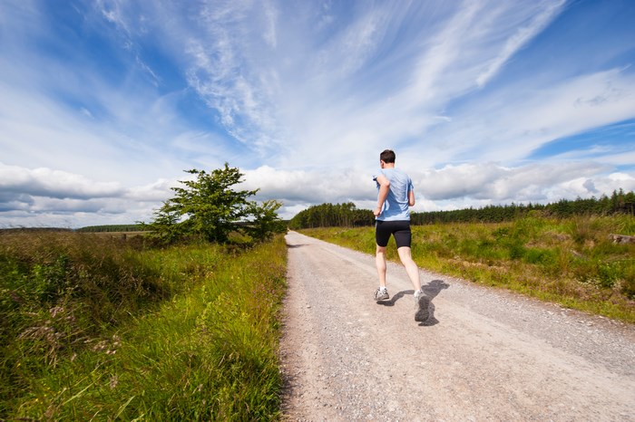Man running on a gravel path through a grassy field