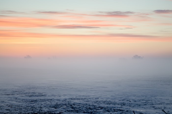 Winter sunrise over a foggy, snow-covered landscape