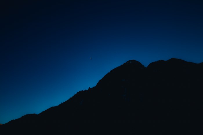 Crescent moon over silhouetted mountain range at night