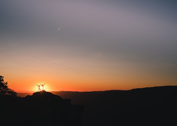 Two people celebrating on a mountain at sunset