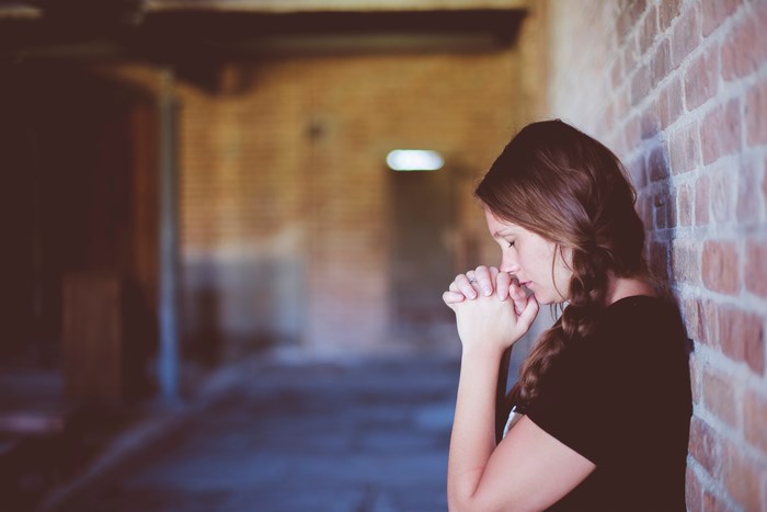 Woman praying leaning against a brick wall
