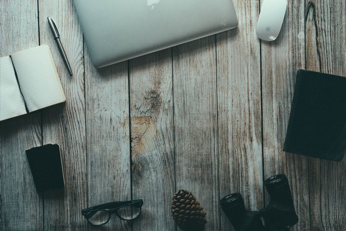Apple MacBook, Notebook, Pen, and Binoculars on Wooden Desk