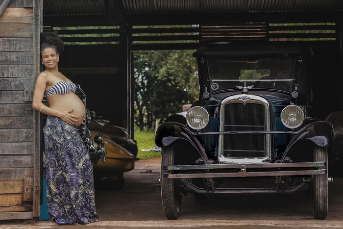 Pregnant woman leaning on a wooden structure next to a classic Chevrolet car