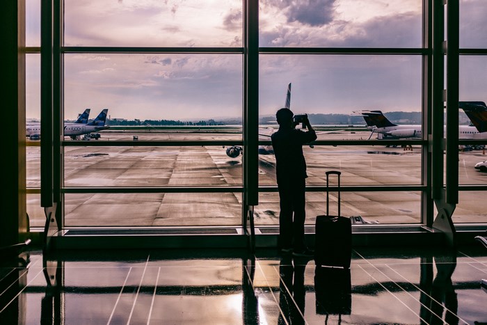 Man with suitcase photographs airplanes at airport terminal