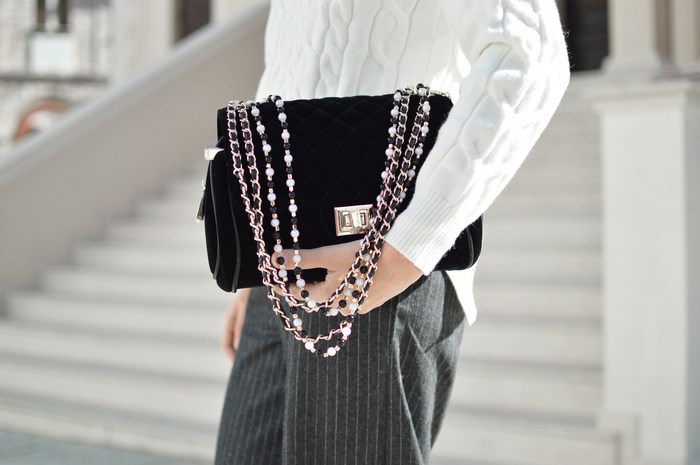 Woman holding a black quilted velvet handbag with beaded chain