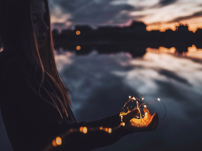 Woman holding fairy lights by the water at sunset