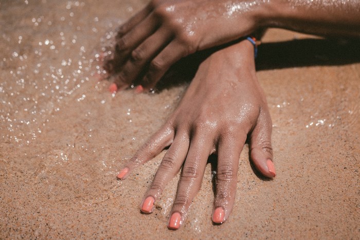 Hands with coral nail polish on wet sand at the beach
