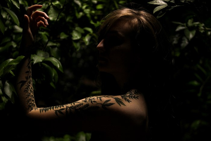 Woman with vine tattoo in dark nature setting