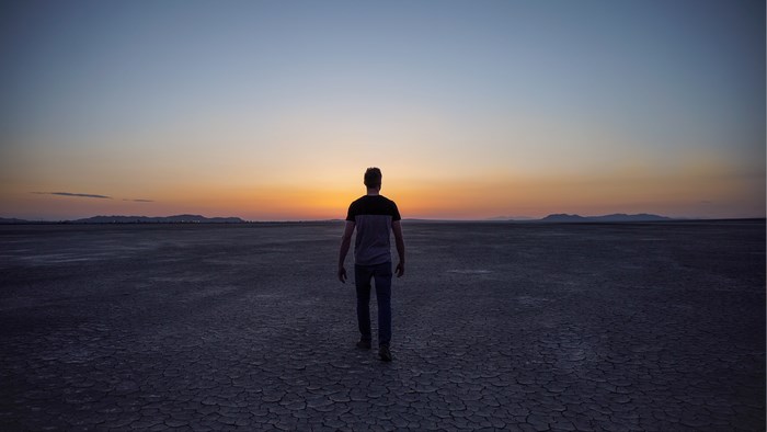 Man walking on dry lake bed at sunset