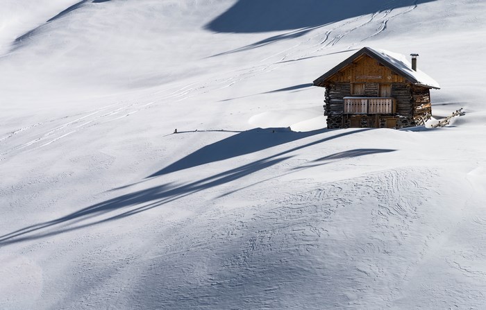 Wooden cabin in a snowy mountain landscape with long shadows