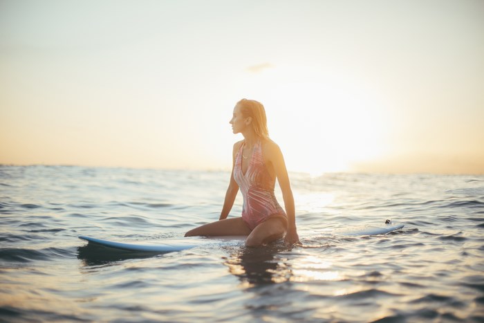 Woman sitting on a surfboard in the ocean at sunset