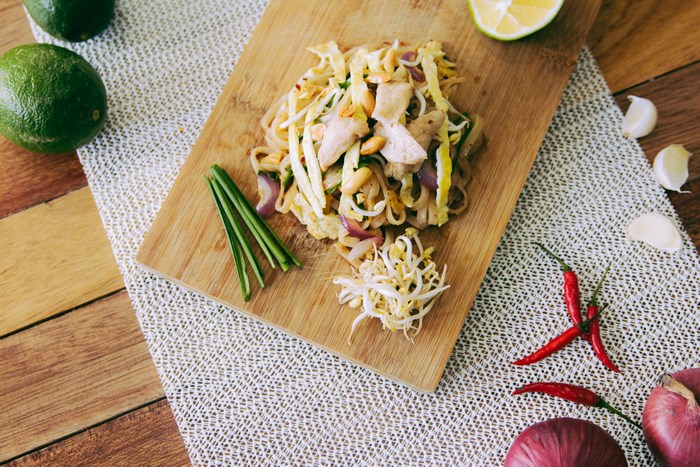Pad Thai with chicken, lime, and chili on a wooden board