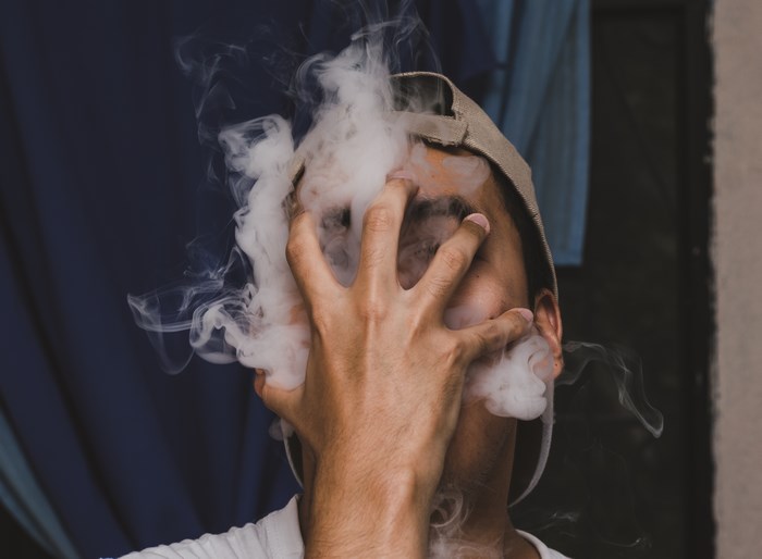 Man wearing a cap exhaling smoke
