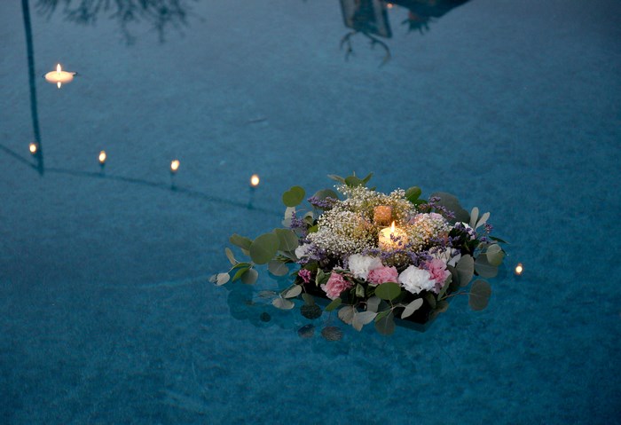 Floating flower bouquet with candles in a pool at dusk