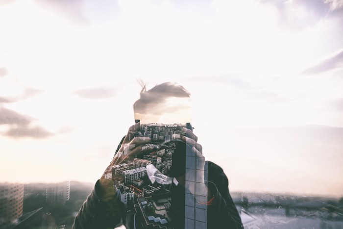 Double exposure of a man holding a Canon camera with a city skyline