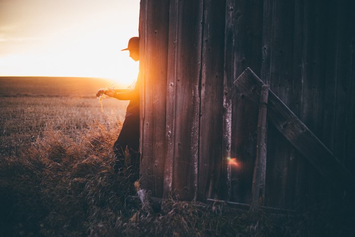 Person in hat by barn at sunset