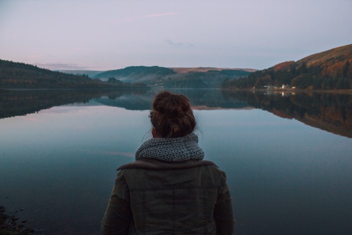 Woman in jacket and scarf looking at a lake