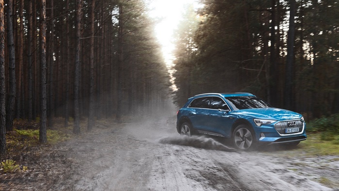 Blue Audi E-tron Quattro driving on a dirt road in a forest