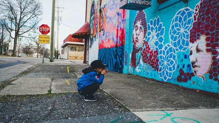 Child photographing a colorful mural on a city street