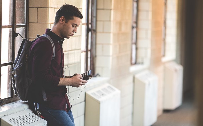 Student with backpack and phone by window