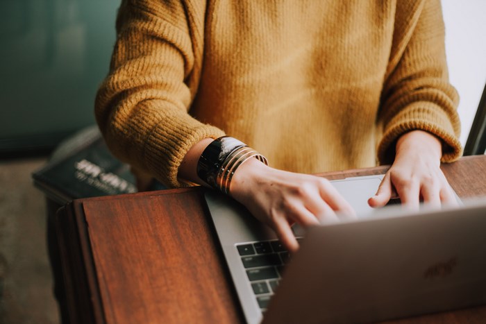 Woman typing on a MacBook wearing a yellow sweater