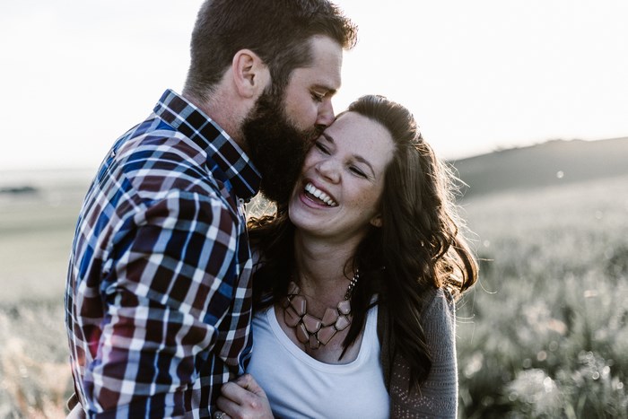 Couple laughing outdoors with man kissing woman's forehead