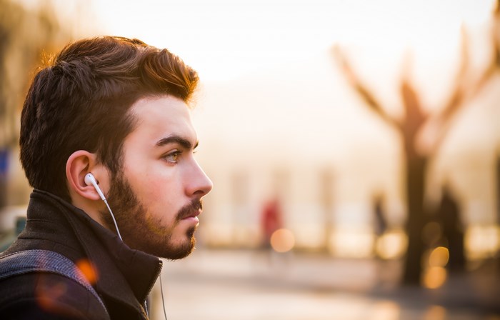 Man with beard listening to music on headphones outdoors