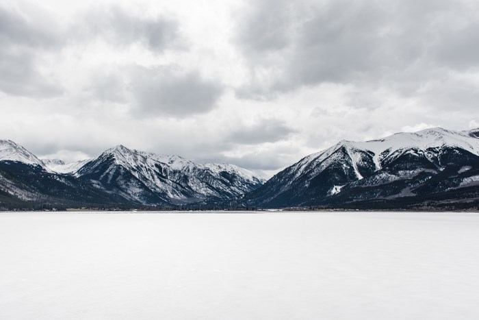 Snow-capped mountains over a frozen lake under cloudy sky