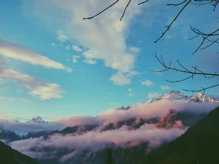 Snowy mountains shrouded in pink clouds under a blue sky