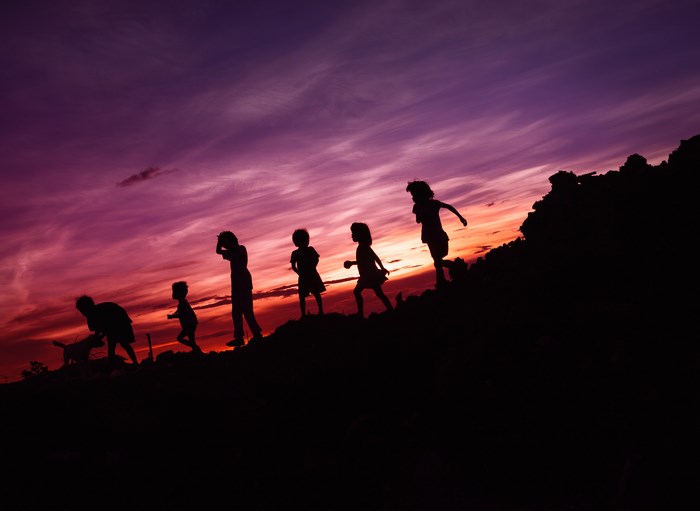 Children and dog silhouetted against a colorful sunset sky