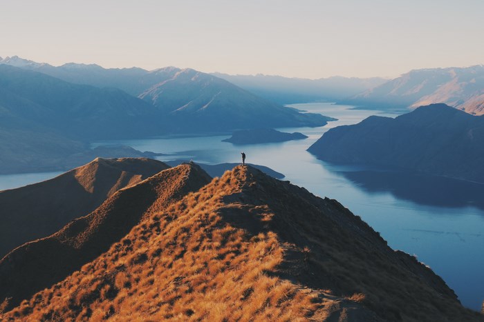 Person standing on mountain ridge overlooking lake and mountains
