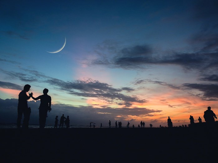 People on beach at sunset with crescent moon