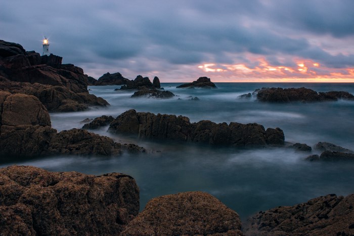 Lighthouse on Rocky Coast at Sunset Overcast Sky