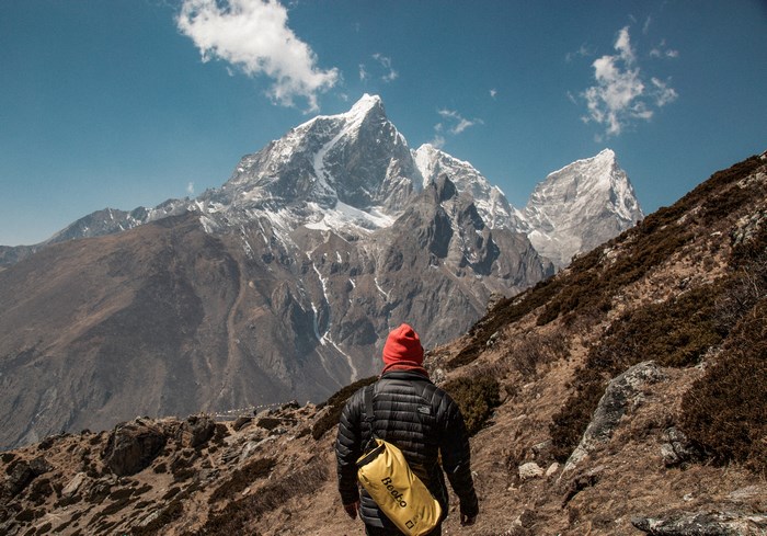 Hiker with yellow bag in front of snowy mountains