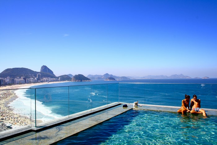 Couple relaxing by infinity pool overlooking Copacabana Beach, Rio de Janeiro