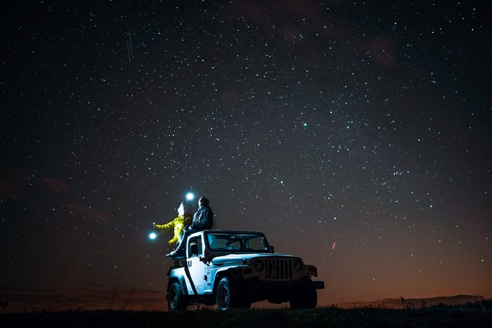 Two people sitting on a Jeep under a starry night sky