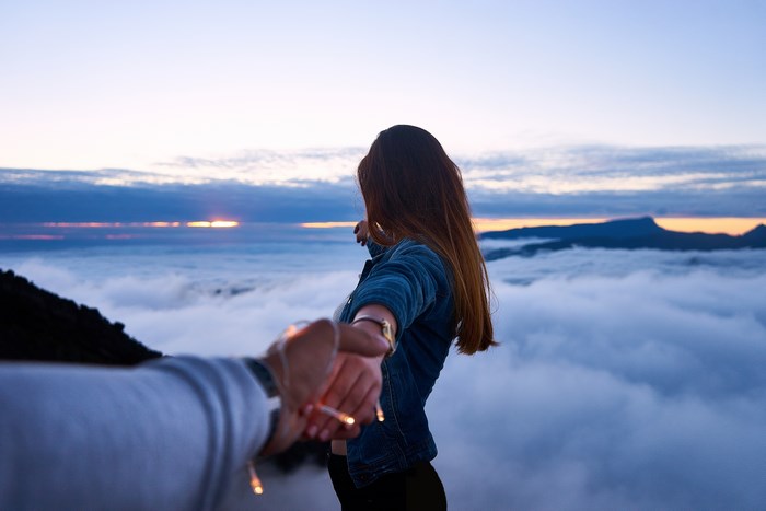 Couple holding hands above clouds at sunrise