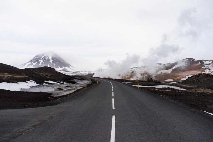 Road through Iceland with snow-capped mountains and steam