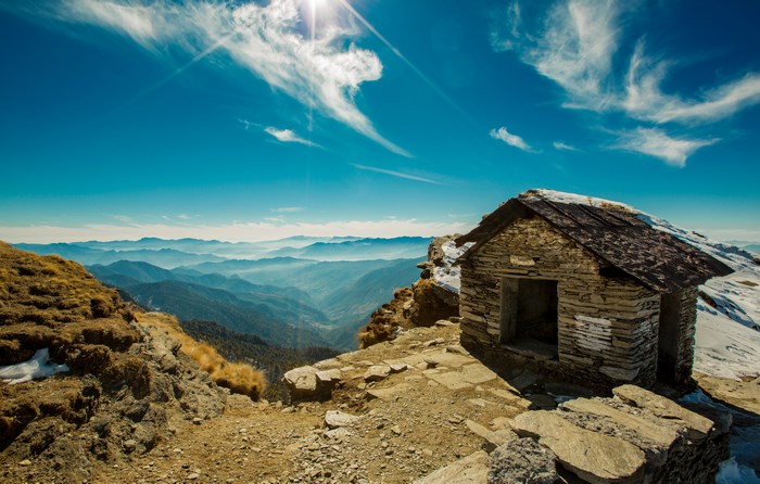 Stone hut on a mountain summit with layered mountain ranges