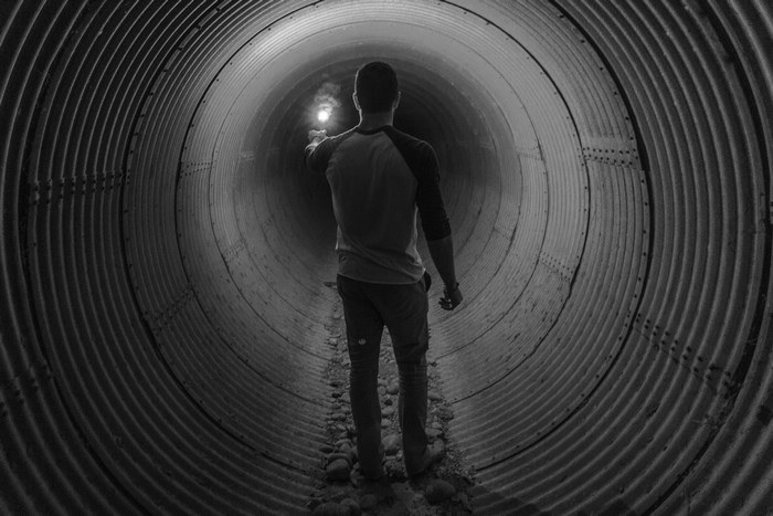Man with flashlight in a corrugated metal tunnel